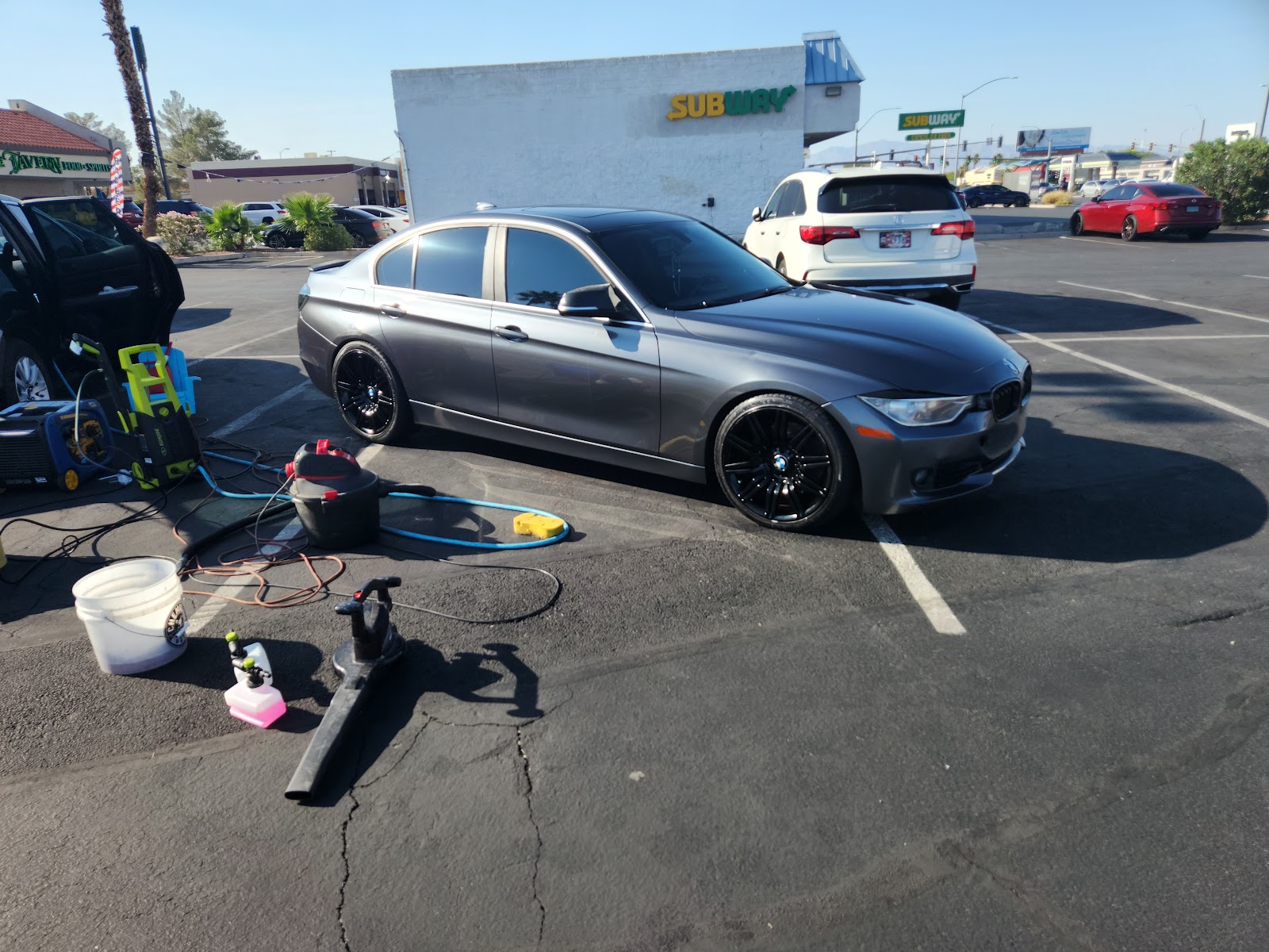 Gray BMW sedan being detailed in a parking lot with equipment nearby